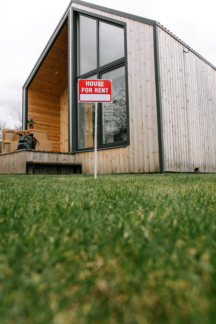 A modern wooden house with a for rent sign on a lush green lawn.
