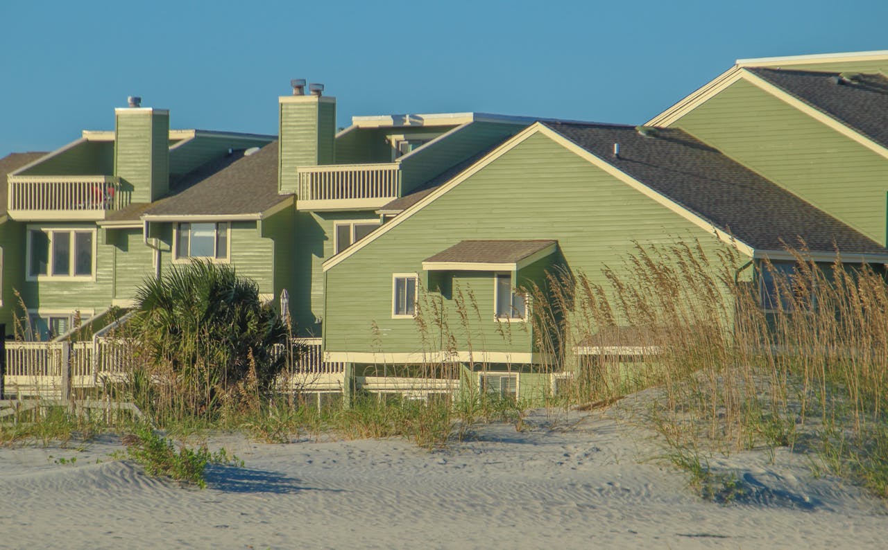 Green vacation homes by the beach with sunny skies and sand dunes.